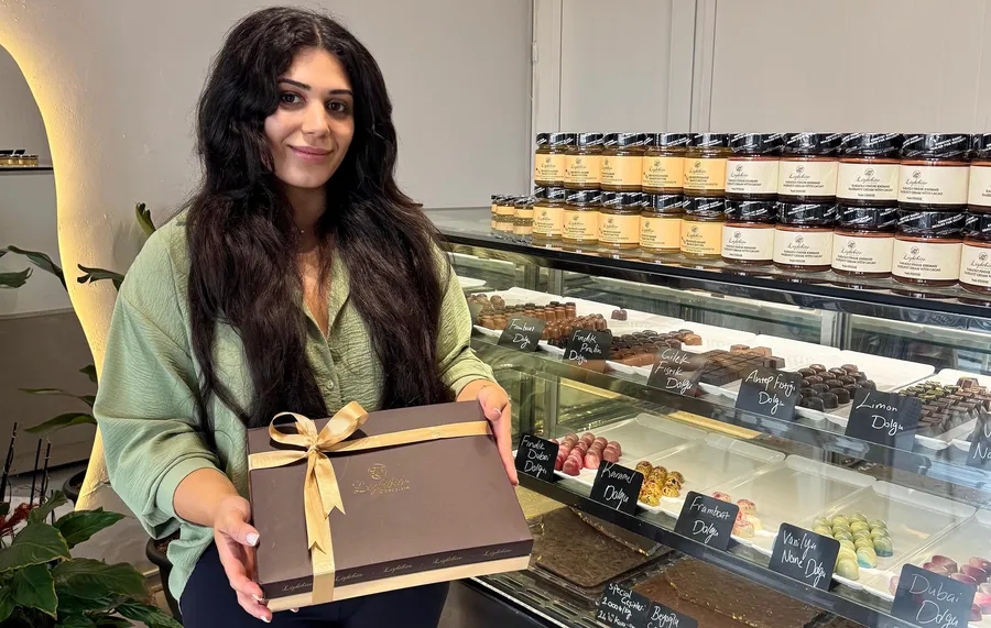 “Bahçekent’te açılan butik çikolata mağazasının sahibi Zahra Alizadeh, elinde şık tasarım çikolata kutusu ile mağazasında poz veriyor. Vitrinde fındık dolgulu, frambuaz dolgulu, hurma özüyle tatlandırılmış sağlıklı ve katkısız özel çikolatalar sergileniyor.”